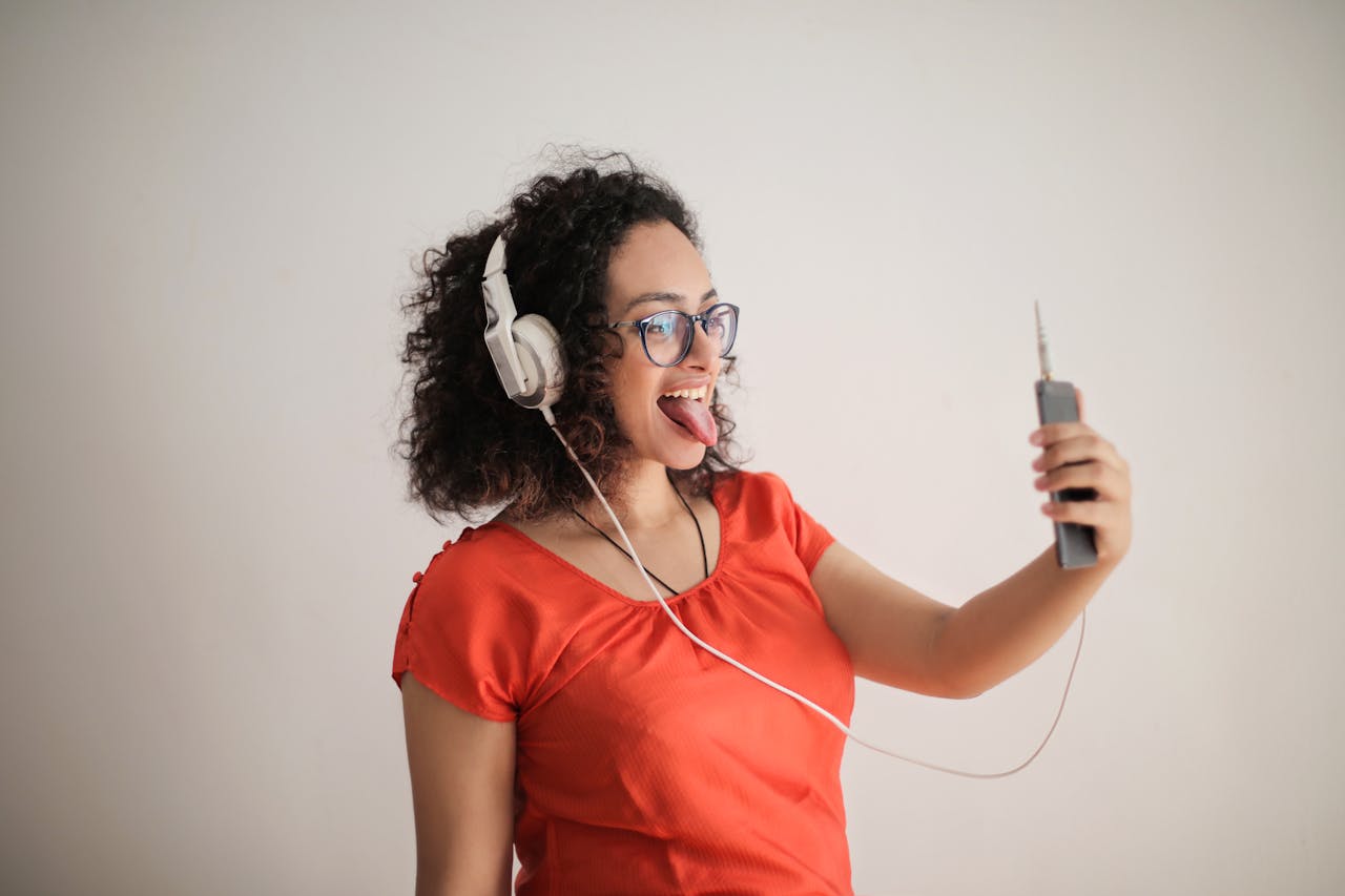 Smiling woman with headphones takes a selfie indoors.
